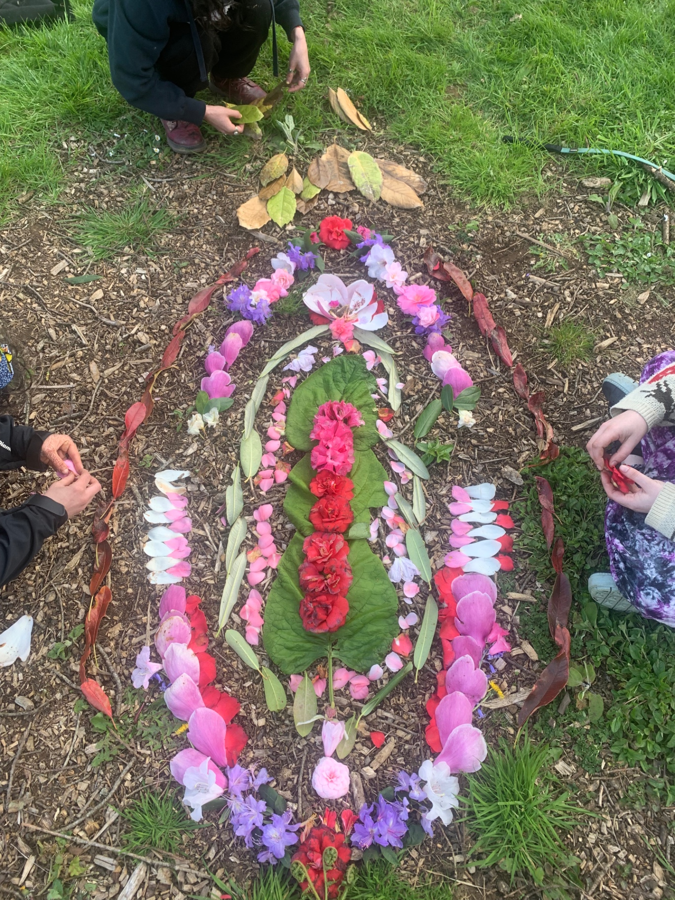 Women arranging flowers and leaves into a ritual mandala on the forest floor.